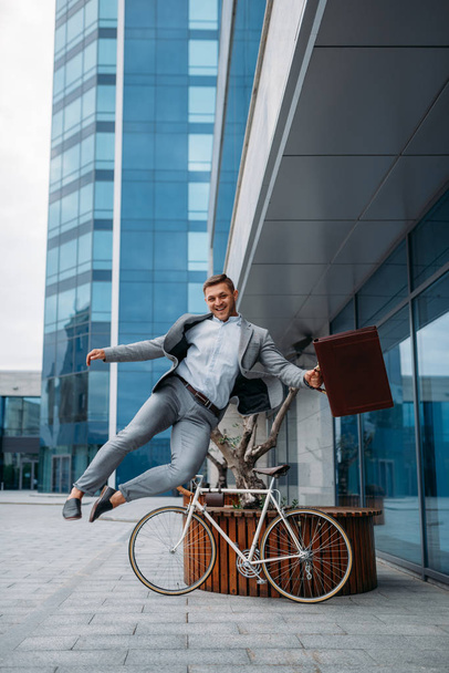 Feliz hombre de negocios con bicicleta en el edificio de oficinas en el centro. Persona de negocios a caballo en el transporte ecológico en la calle de la ciudad, estilo urbano
 - Foto, imagen