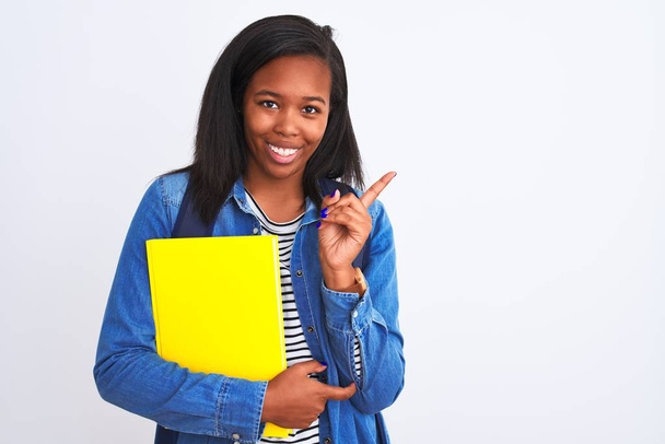 Young african american student woman wearing backpack and book over isolated background very happy pointing with hand and finger to the side - Фото, изображение