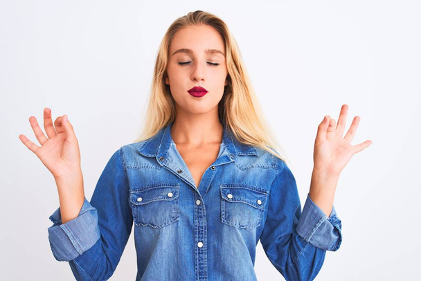 Young beautiful woman wearing casual denim shirt standing over isolated white background relaxed and smiling with eyes closed doing meditation gesture with fingers. Yoga concept. - Photo, Image