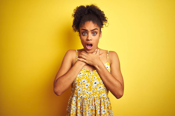 Afro-Amerikaanse vrouw draagt casual bloemenjurk staan over geïsoleerde gele achtergrond schreeuwen stikken omdat pijnlijke wurging. Gezondheidsproblemen. Verstikking en zelfmoordconcept. - Foto, afbeelding