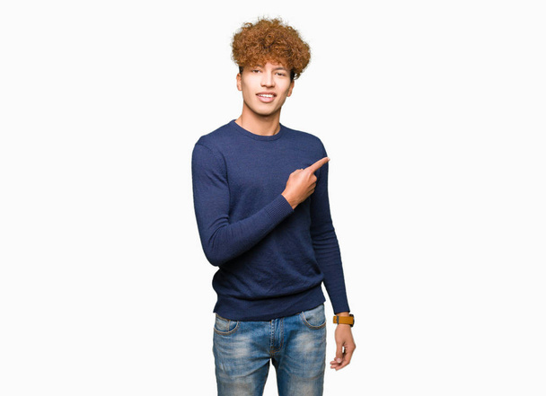 junger gutaussehender Mann mit Afro-Haaren, der mit dem Finger zur Seite zeigt und Werbung zeigt, ernstes und ruhiges Gesicht - Foto, Bild