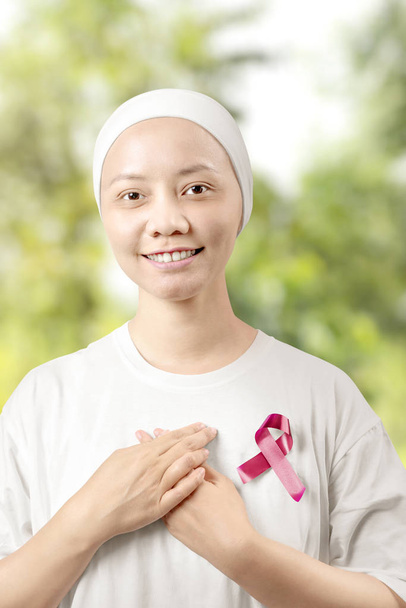 Asian woman in a white shirt with a pink ribbon with a green par - Фото, изображение