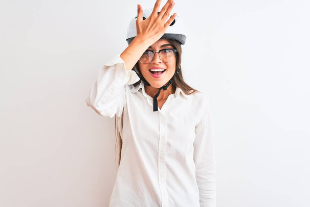 Beautiful businesswoman wearing glasses and bike helmet over isolated white background surprised with hand on head for mistake, remember error. Forgot, bad memory concept. - Foto, Bild