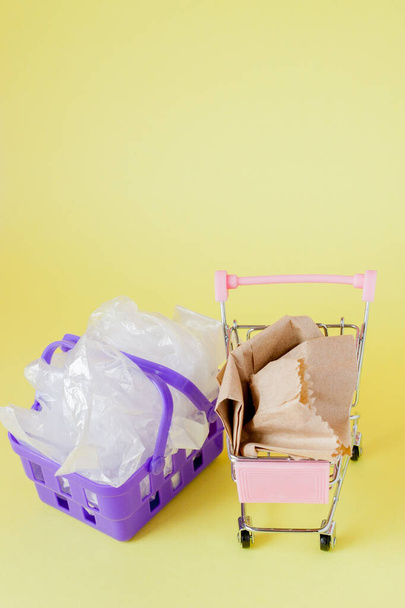 πολυθαλίνη και χάρτινες σακούλες σε ένα καλάθι αγορών σε ένα κίτρινο πίσω - Φωτογραφία, εικόνα