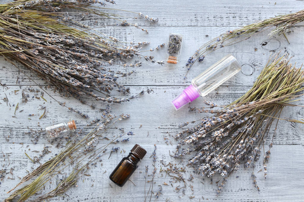 Dry natural lavender flowers, bottles with buds, essential lavender oil, organic perfume spray over wooden background - Fotó, kép