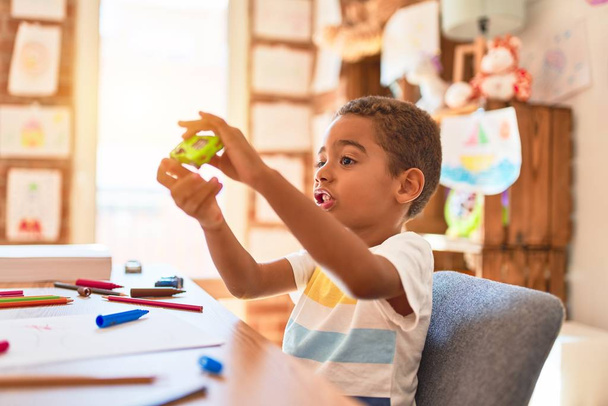 Beautiful african american toddler sitting on desk playing with cars at kindergarten - Foto, Bild