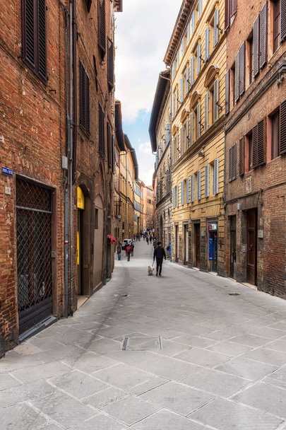 SIENA, ITALY - APRIL 9, 2019: Tourists are walking trough the narrow medieval streets in Siena, Italy - 写真・画像