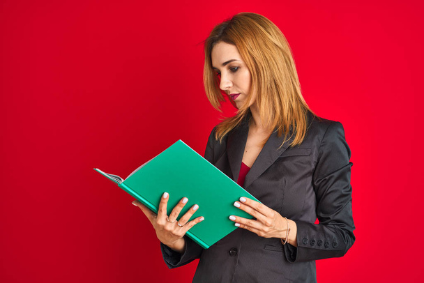 Young beautiful redhead businesswoman wearing suit reading book - Valokuva, kuva