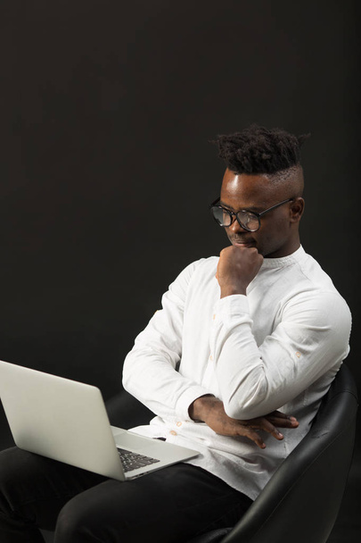 handsome african man in glasses with laptop on black background - 写真・画像
