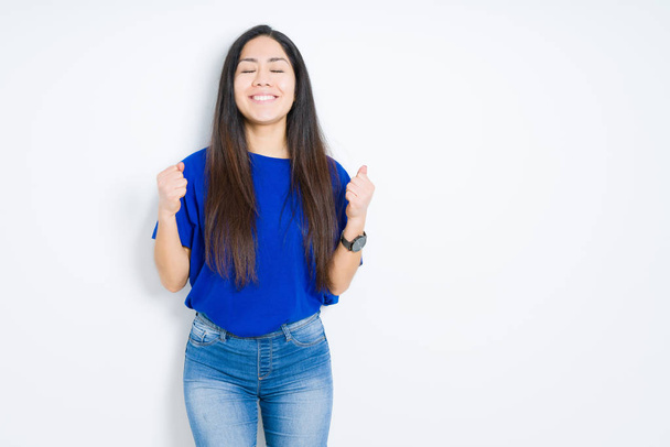 Beautiful brunette woman over isolated background very happy and excited doing winner gesture with arms raised, smiling and screaming for success. Celebration concept. - Photo, Image