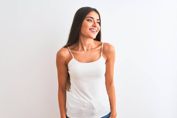 ●カジュアルなTシャツを着た若い美人女性が、笑顔で横を向く孤立した白い背景の上に立ち、自然な表情。自信を持って笑う. - 写真・画像