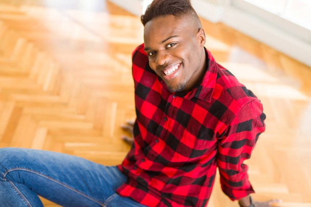 Красивий африканський молодий чоловік посміхається впевнено сидячи на підлозі з великою посмішкою на обличчі
 - Фото, зображення