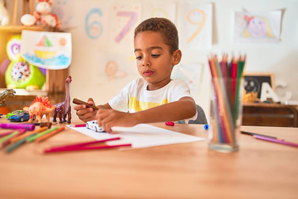 Beautiful african american toddler sitting painting car toy using marker pen on desk at kindergarten - 写真・画像