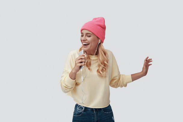 Attraktive junge Frau hört Musik und lächelt vor grauem Hintergrund - Foto, Bild