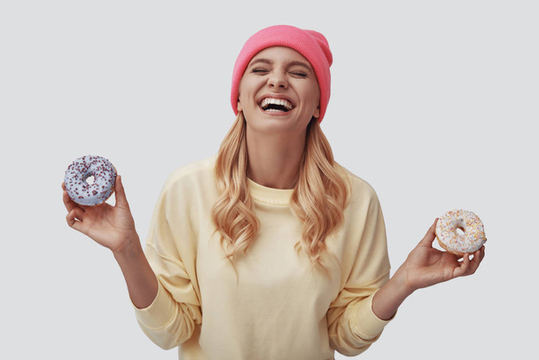 Attractive young woman holding donuts and smiling while standing against grey background - Fotoğraf, Görsel