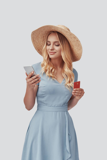 Attrayant jeune femme souriant et acheter quelque chose en ligne tout en se tenant debout sur fond gris
  - Photo, image