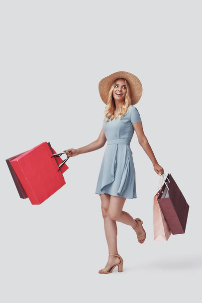 Houkuttelevan nuoren naisen koko pituus hymyilee ja kantaa ostoskasseja harmaata taustaa vasten
  - Valokuva, kuva