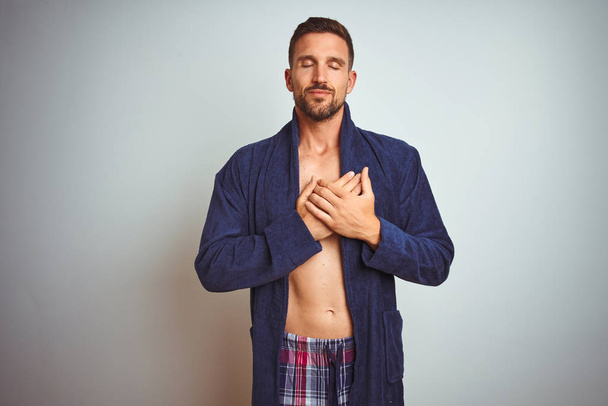 Σέξι shirtless άνθρωπος φορώντας άνετα πιτζάμες και ρόμπα πάνω από απομονωμένη φόντο χαμογελώντας με τα χέρια στο στήθος με κλειστά μάτια και ευγνώμων χειρονομία στο πρόσωπο. Έννοια υγείας. - Φωτογραφία, εικόνα