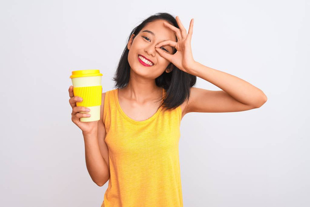 Jeune femme chinoise boire emporter verre de café sur fond blanc isolé avec le visage heureux souriant faire ok signe avec la main sur l'oeil regardant à travers les doigts
 - Photo, image