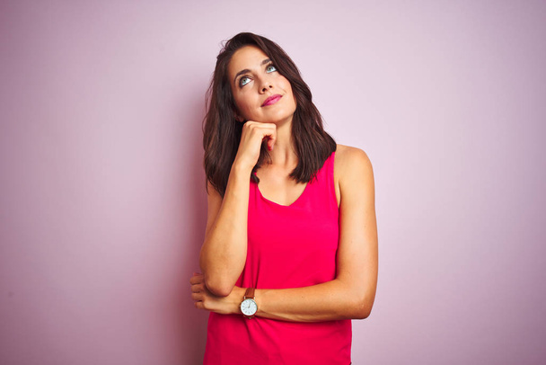 Young beautiful woman wearing t-shirt standing over pink isolated background with hand on chin thinking about question, pensive expression. Smiling with thoughtful face. Doubt concept. - Foto, imagen