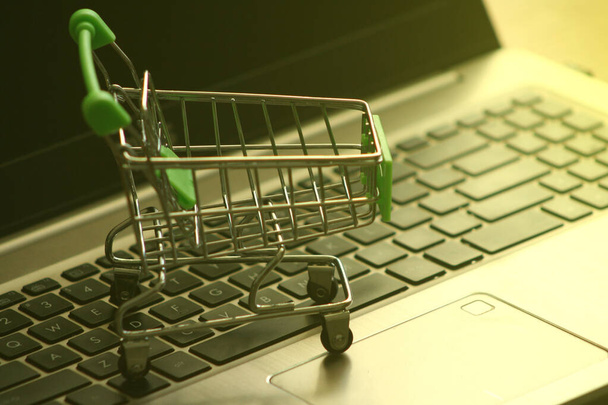 A mini dummy shopping trolley on a lapptop keyboard as a concept for online shopping, saving, business and making money as well as running a business. - Photo, Image