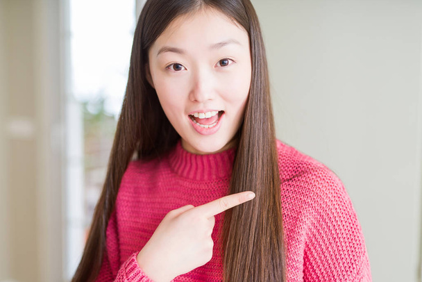 Красива Азіатська жінка носить рожевий светр веселий з посмішкою особа вказуючи з рук і пальцем до сторони з щасливим і природним виразом на обличчі - Фото, зображення