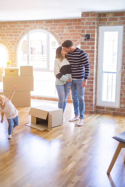 Beautiful family with a kid standing at new home around cardboard boxes - Photo, Image
