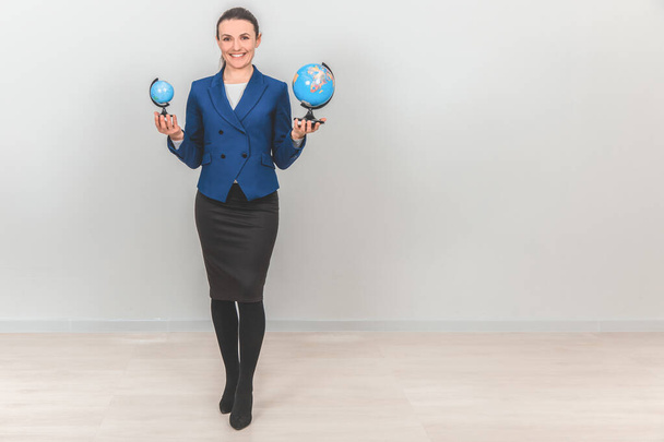 Pretty geography teacher holding two globes, one big and one small, smiling. - Foto, afbeelding