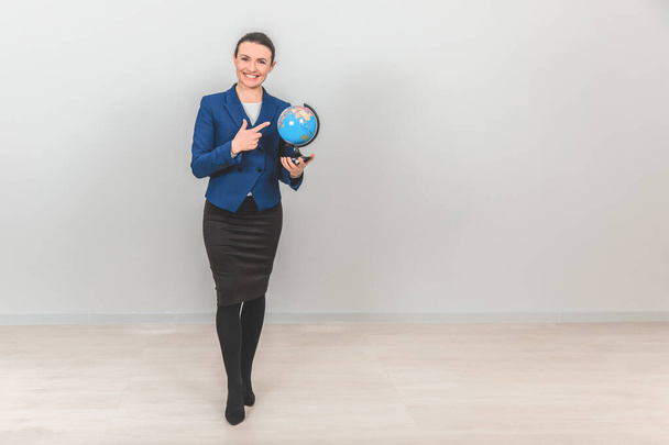 Young geography teacher holding a globe, pointing her finger at it, smiling. - Foto, afbeelding