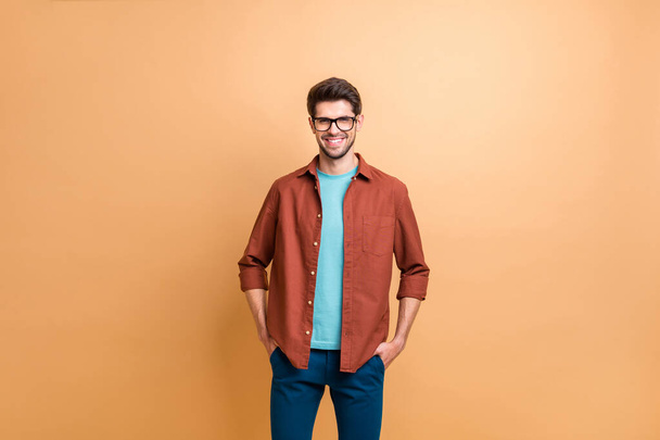 Portrait of his he nice attractive trendy cheerful cheery experienced brunet guy holding hands in pockets isolated over beige color pastel background - Zdjęcie, obraz