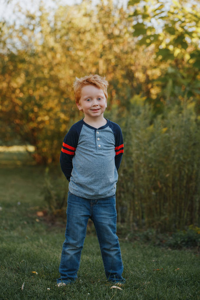 Portrait of Caucasian red-haired cute handsome preschool boy. Adorable child standing outside on autumn fall day. Happy smiling kid outdoor. Authentic lifestyle childhood. - Foto, Bild