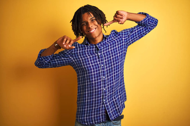 Afro férfi raszta visel alkalmi ing felett áll elszigetelt sárga háttér mosolyogva vidám bemutató és rámutatva ujjal fogak és száj. Fogászati egészség fogalma. - Fotó, kép