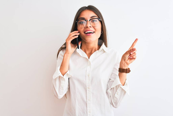 Jeune femme d'affaires portant des lunettes parlant sur smartphone sur fond blanc isolé très heureux pointant avec la main et le doigt sur le côté
 - Photo, image