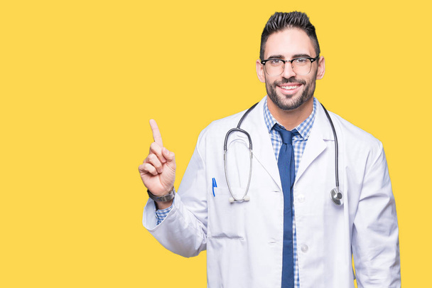Handsome young doctor man over isolated background with a big smile on face, pointing with hand and finger to the side looking at the camera. - Photo, Image