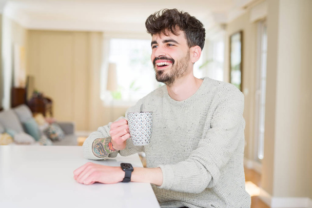 schöner junger Mann, der zu Hause eine Tasse Kaffee trinkt und - Foto, Bild
