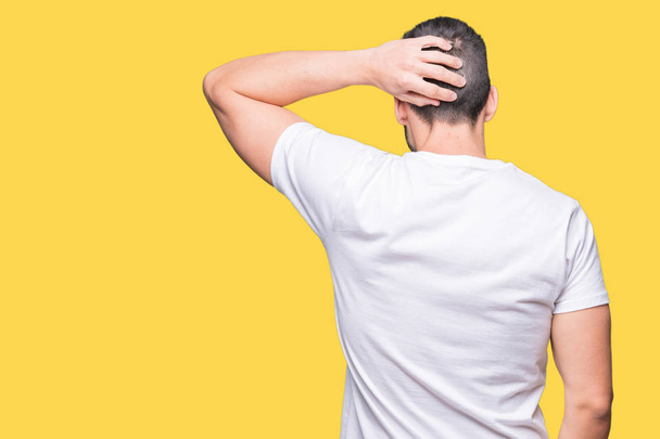 Красивый мужчина в белой футболке на желтом изолированном фоне задом наперед думает о сомнении с рукой на голове
 - Фото, изображение