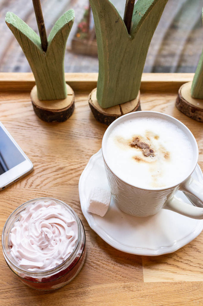 Top view of latte or cappuccino in a white cup, strawberry cream cheese dessert and smart phone on wooden table in cafe. - Valokuva, kuva