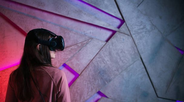 Portrait of a girl, a woman in virtual reality glasses, against the background of a concrete wall, backlit by neon. - Foto, Bild