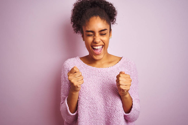 Jonge Afro-Amerikaanse vrouw draagt winter trui staan over geïsoleerde roze achtergrond opgewonden voor succes met opgeheven armen en ogen gesloten vieren overwinning glimlachen. Winnaars concept. - Foto, afbeelding