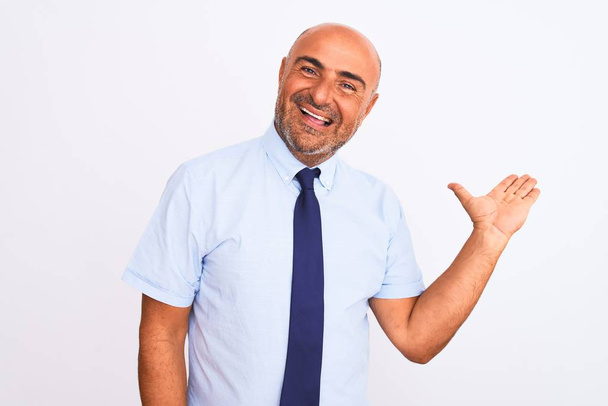 Middle age businessman wearing tie standing over isolated white background smiling cheerful presenting and pointing with palm of hand looking at the camera. - Foto, afbeelding