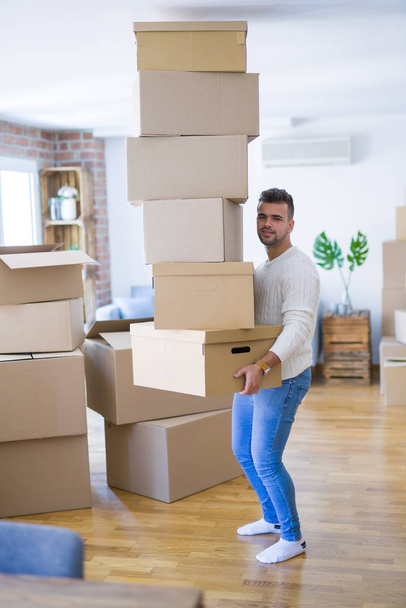 Joven hombre guapo mudándose a un nuevo apartamento, sosteniendo una pila de cajas de cartón, feliz por un nuevo hogar
 - Foto, Imagen