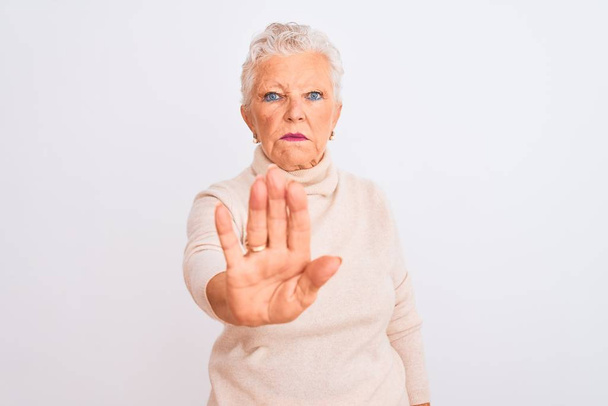 Senior grijs-harige vrouw draagt coltrui staan over geïsoleerde witte achtergrond doen stoppen met zingen met palm van de hand. Waarschuwingsuitdrukking met negatief en ernstig gebaar op het gezicht. - Foto, afbeelding