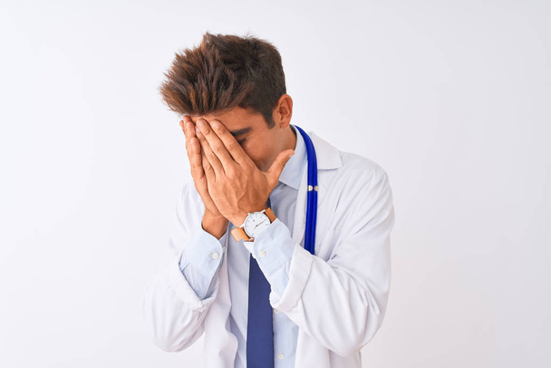Mladý pohledný lékař ve stetoskopu na izolovaném bílém pozadí se smutným výrazem, zakrývajícím tvář rukama při pláči. Koncept deprese. - Fotografie, Obrázek