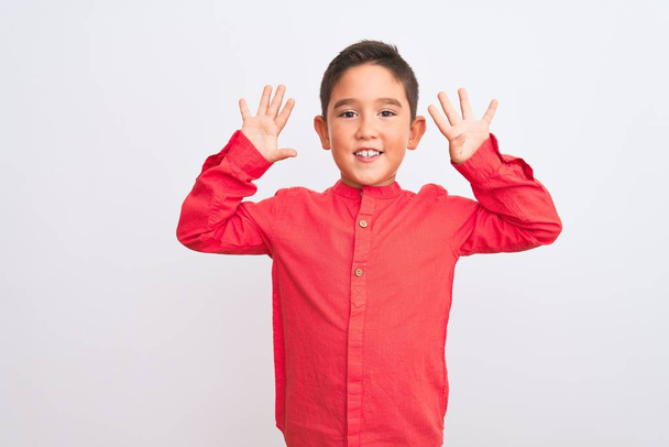Красивый мальчик в элегантной красной рубашке стоит на изолированном белом фоне показывая и показывая пальцами номер девять улыбаясь уверенно и счастливо
. - Фото, изображение