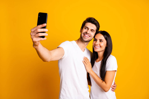 Photo of two people holding telephone in hand taking selfies for new post wear casual clothes isolated yellow color background - Valokuva, kuva