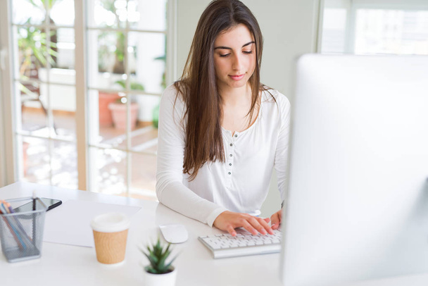 Kaunis nuori liiketoiminnan nainen työskentelee tietokoneella, hymyillen ja keskittyen online-työhön
 - Valokuva, kuva