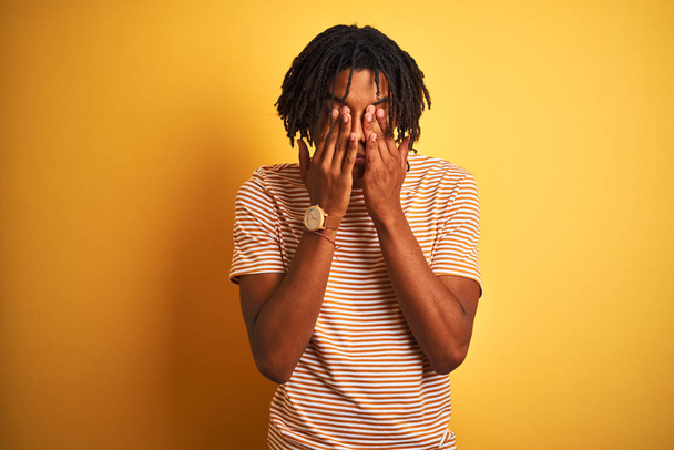 Афро-чоловік з дредлоками носить смугасту футболку, що стоїть над ізольованим жовтим тлом, натираючи очі на втому і головний біль, сонний і втомлений вираз. Проблема зору
 - Фото, зображення