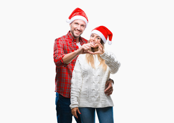 Casal jovem apaixonado vestindo chapéu de Natal sobre fundo isolado sorrindo no amor mostrando símbolo do coração e forma com as mãos. Conceito romântico
. - Foto, Imagem