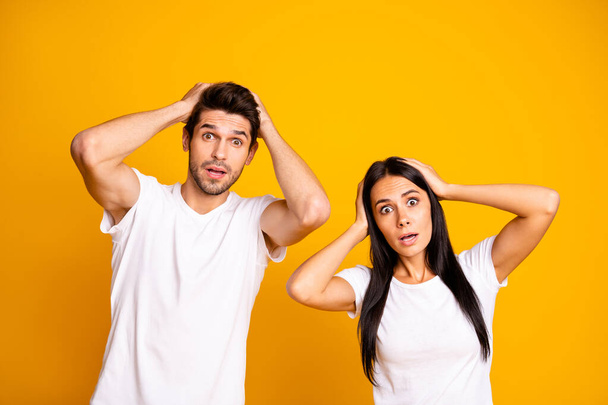 Photo of nice couple holding hands on head not believe bad news wear casual white t-shirts isolated yellow color background - Photo, Image