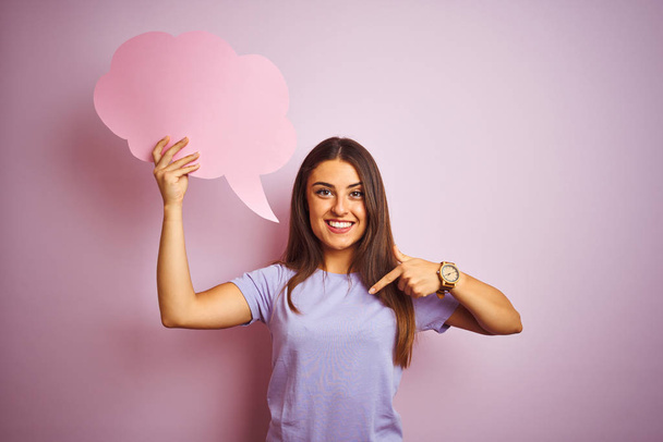 Young beautiful woman holding cloud speech bubble over isolated pink background with surprise face pointing finger to himself - Foto, Bild